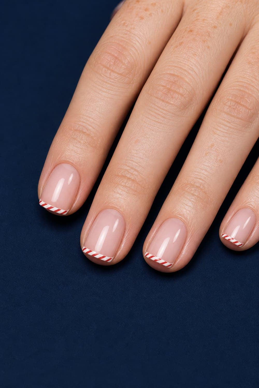 Short square Christmas nails with a sheer pink base and thin red-and-white candy cane French tips.