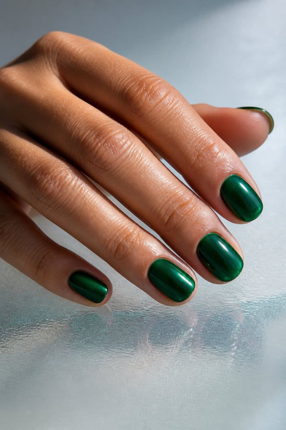 Short oval Christmas nails in translucent emerald green glass polish with a glossy finish.