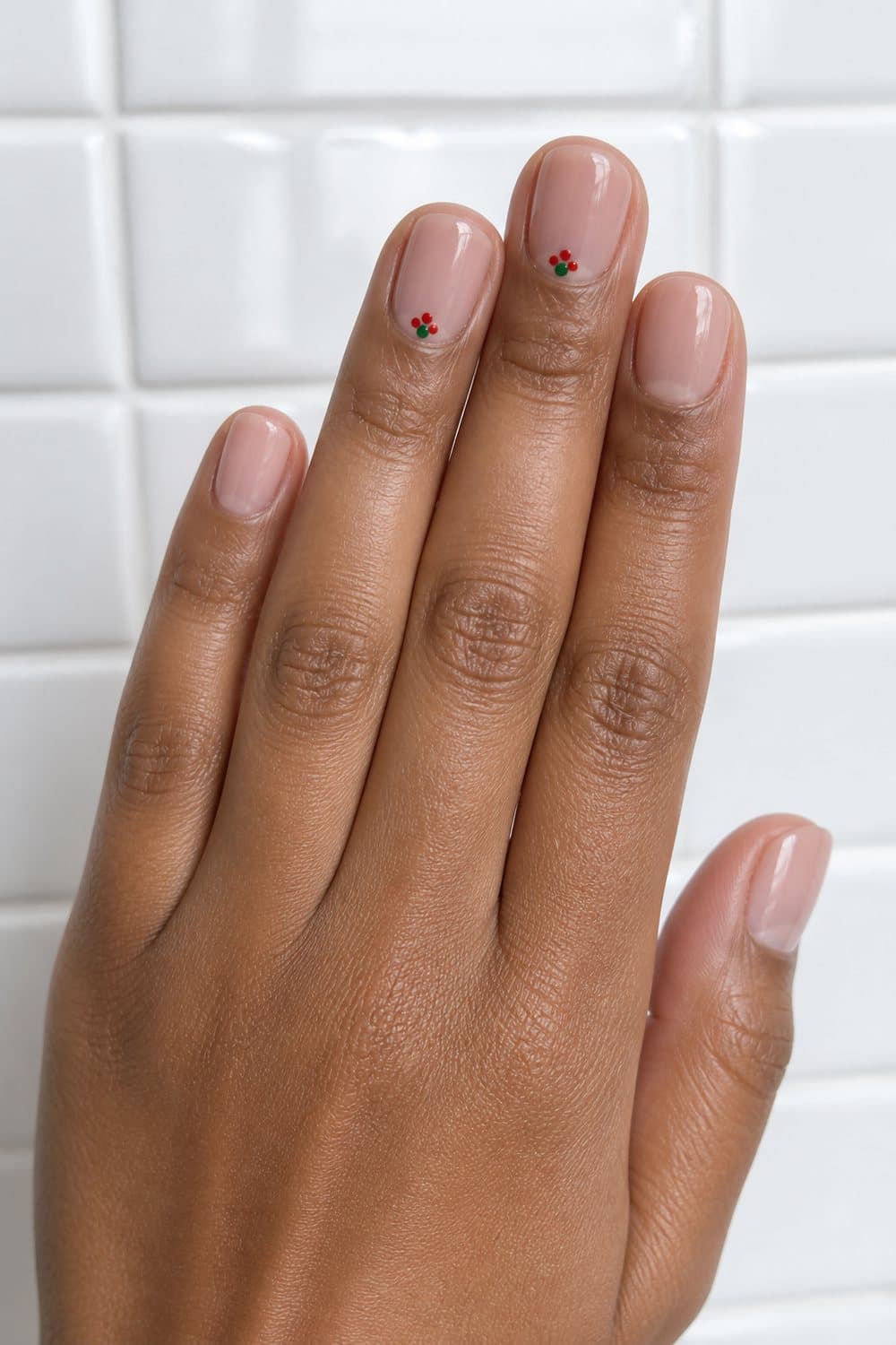 Short round Christmas nails with a sheer nude base and tiny red-and-green holly dot accents.