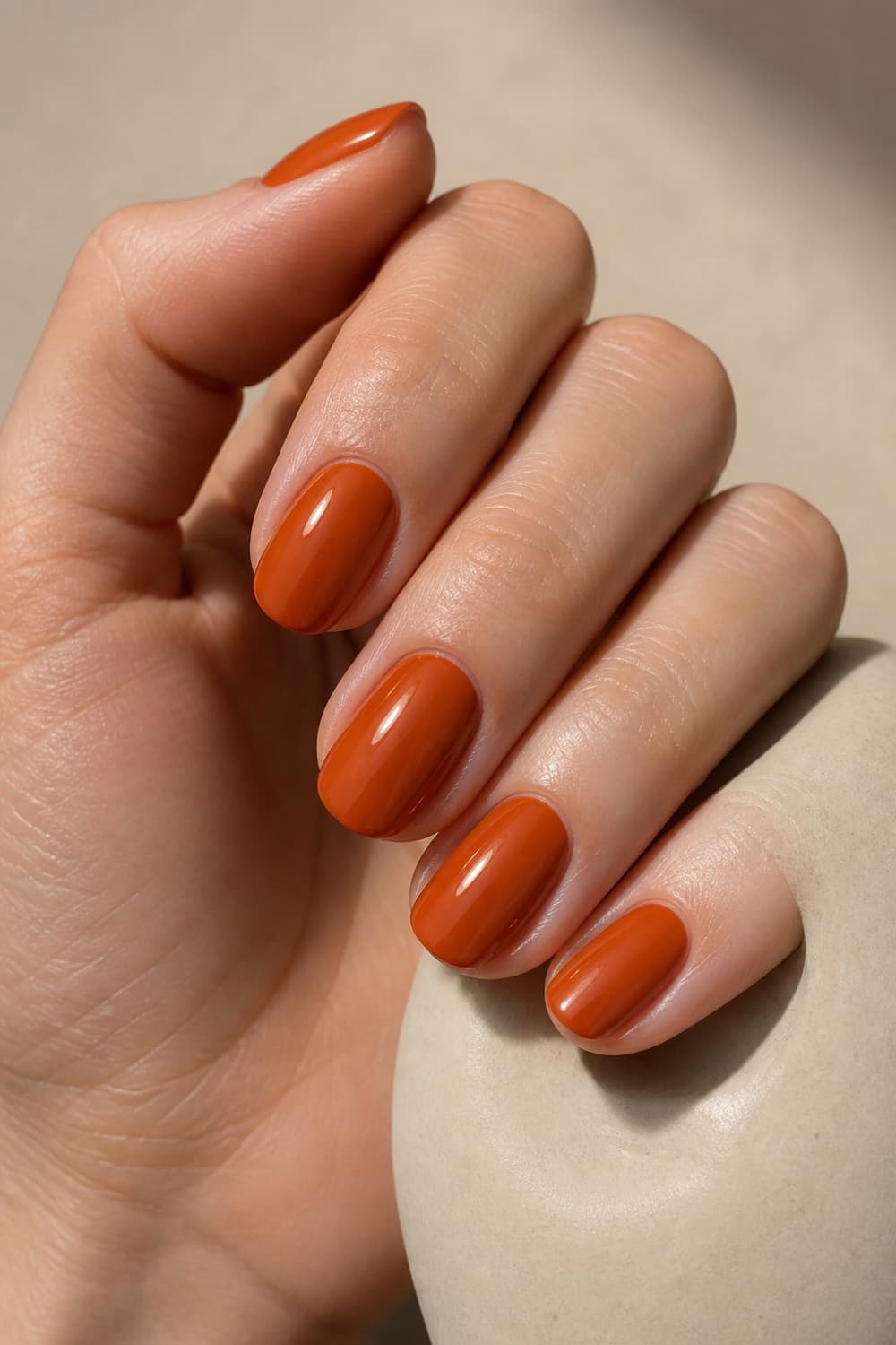 Glossy burnt orange oval nails in warm fall light