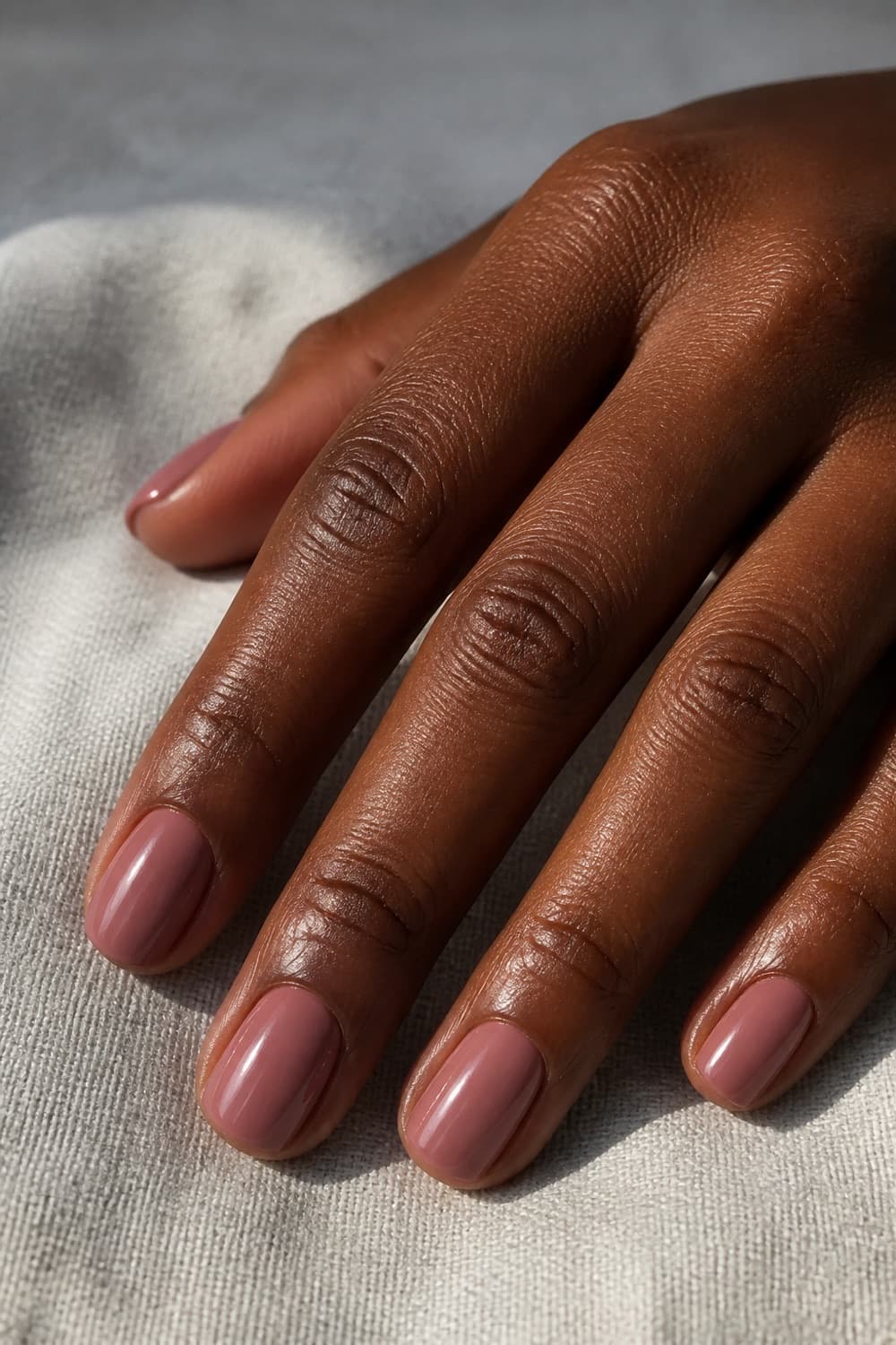 Short squoval dried rose nails with a glossy fall finish on a deep skin tone