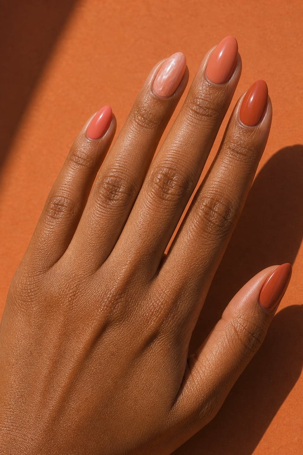 Coral-to-terracotta tonal August manicure with one pearl accent on soft almond nails