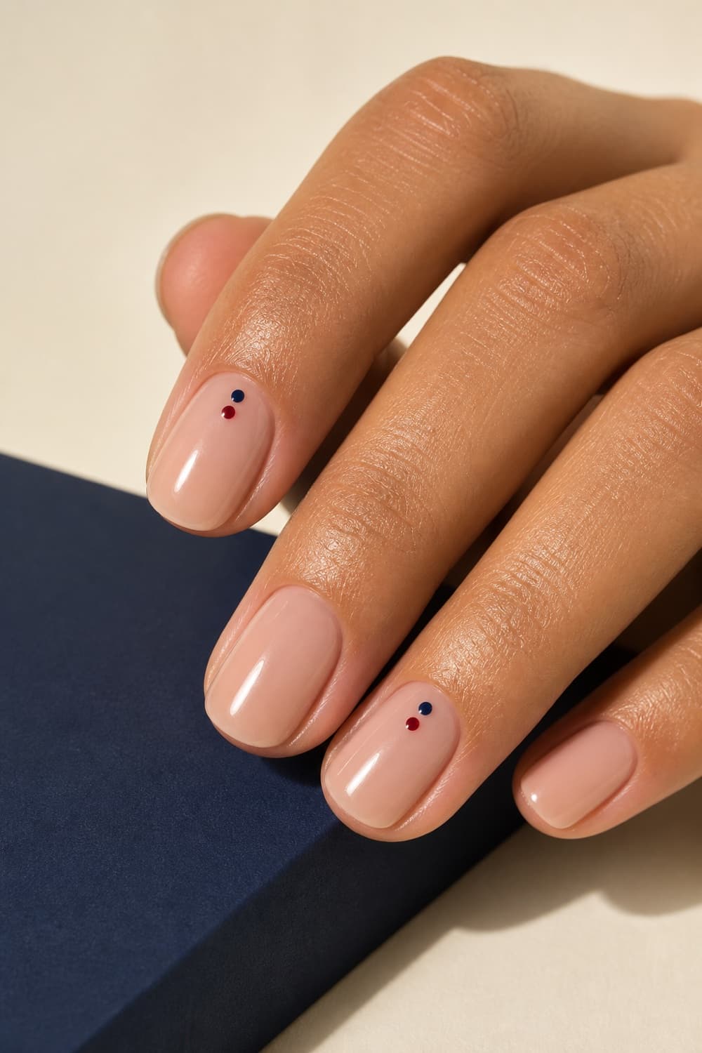 Short sheer nails with tiny navy and red school-color dot accents near the cuticle