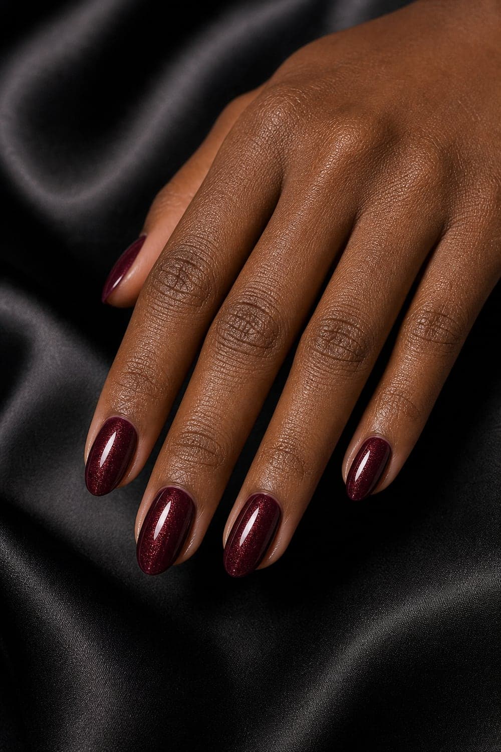 Ultra realistic burgundy manicure with gold shimmer on a close-up hand