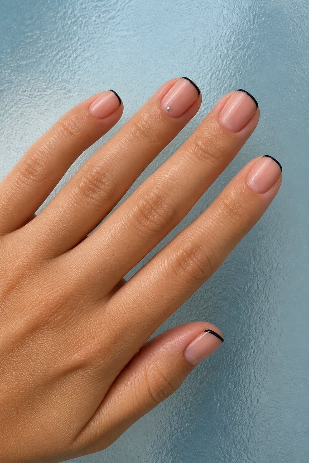 Short squoval nails with a sheer nude base, ultra-thin black French tips, and one tiny silver dot accent