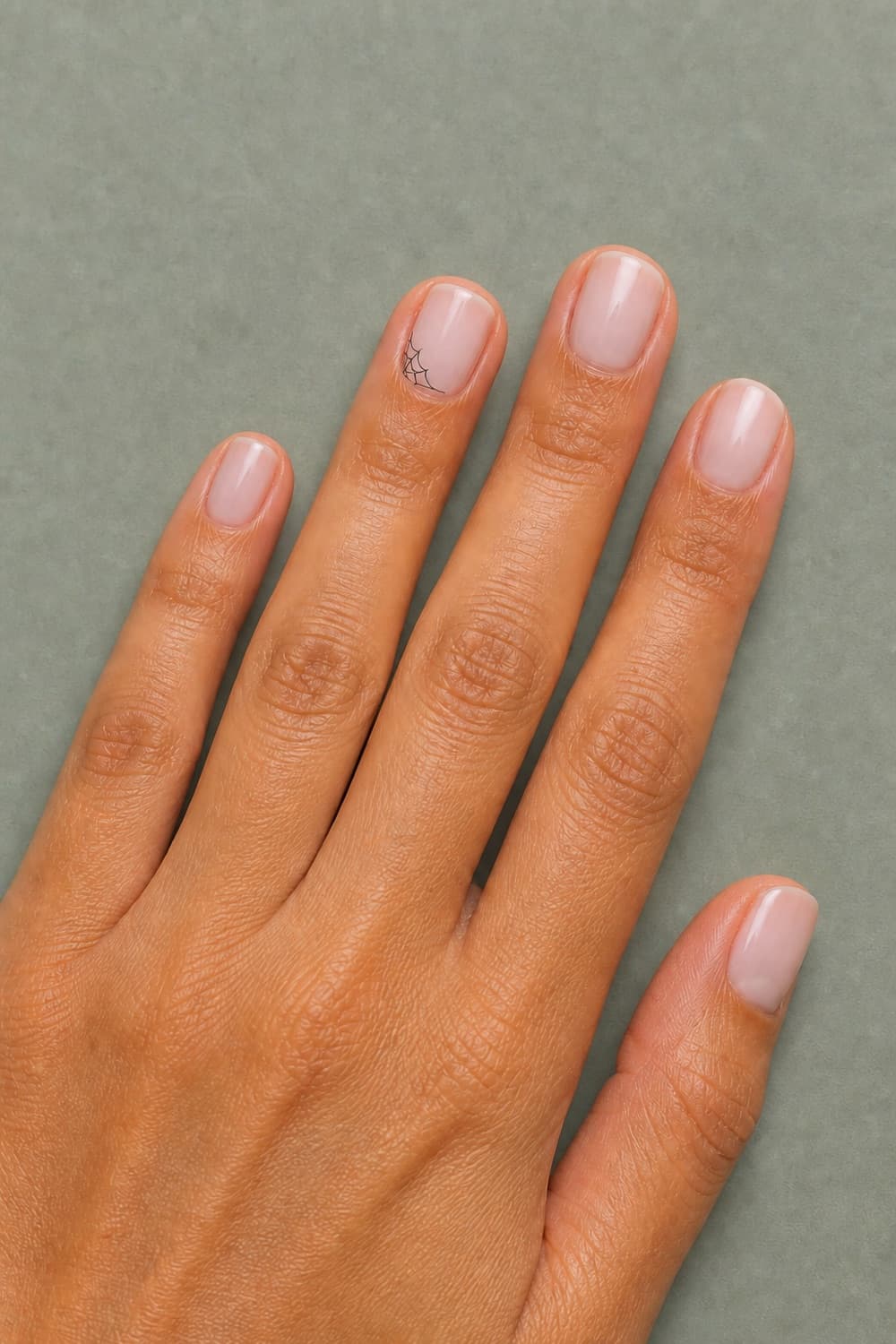 Short square milky nails with one fine black spiderweb corner accent