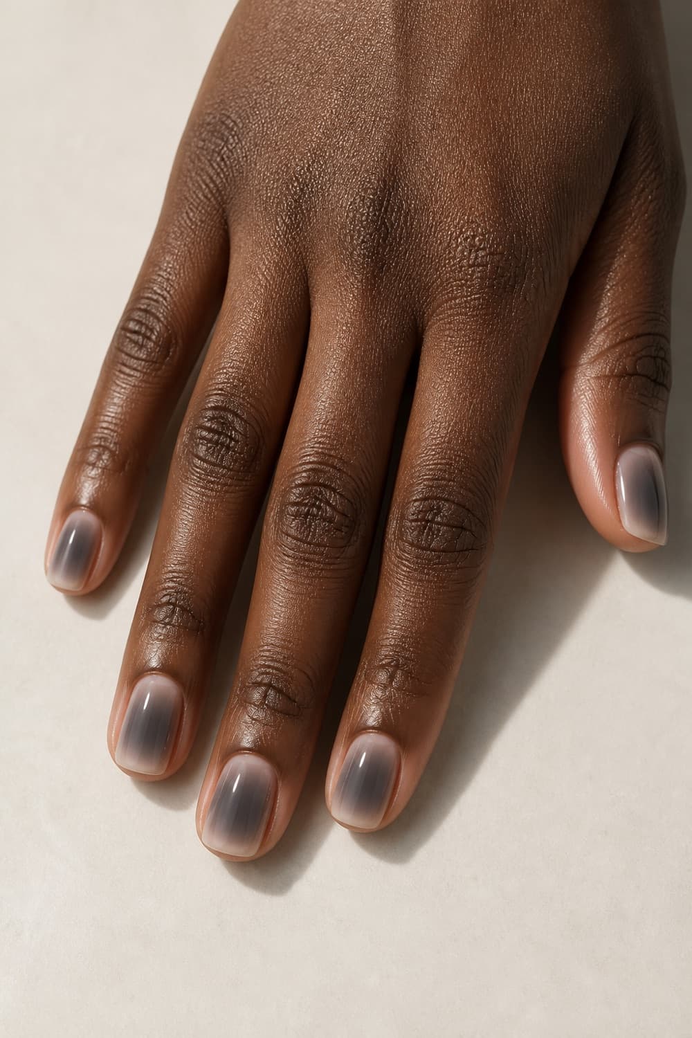 Short squoval nails with a smoky grey aura over a translucent neutral base